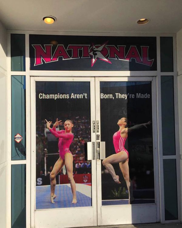 National gym window vinyl with gymnasts and slogan “Champions Aren’t Born, They’re Made.”