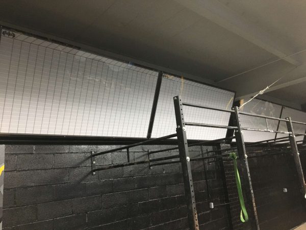 Grid-style perforated vinyl covering upper gym windows above black wall.
