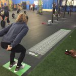 Athlete prepares to jump on a floor-mounted broad jump measurement decal in a CrossFit gym.
