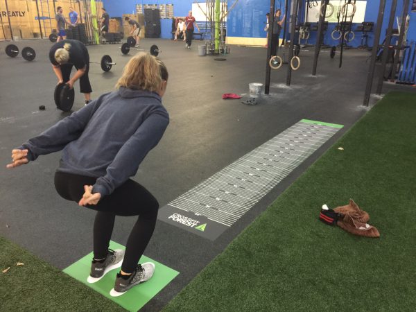 Athlete prepares to jump on a floor-mounted broad jump measurement decal in a CrossFit gym.