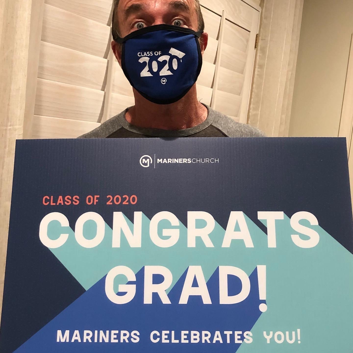 Man with Class of 2020 mask holding a graduation yard sign