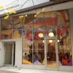 Storefront with geometric window decals in red, yellow, blue, and purple tones.