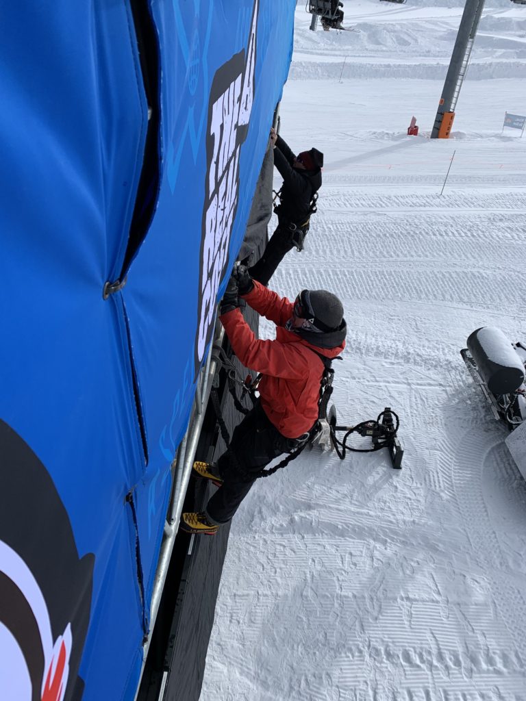 Technicians installing large banner on snowy outdoor event structure