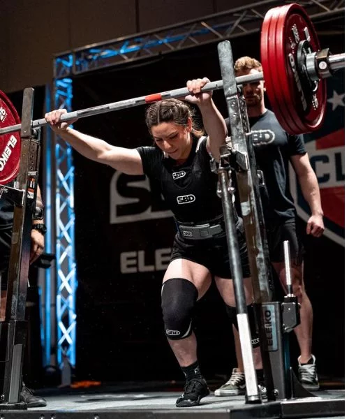 Female powerlifter setting up under a loaded barbell at competition